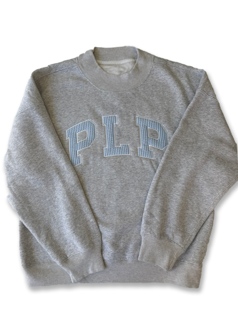 A heather gray crewneck sweatshirt featuring the letters 'PLP' in light blue and white striped varsity block letters across the chest, laid flat against a white background.