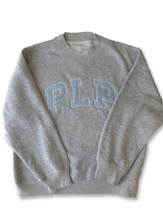 A heather gray crewneck sweatshirt featuring the letters 'PLP' in light blue and white striped varsity block letters across the chest, laid flat against a white background.